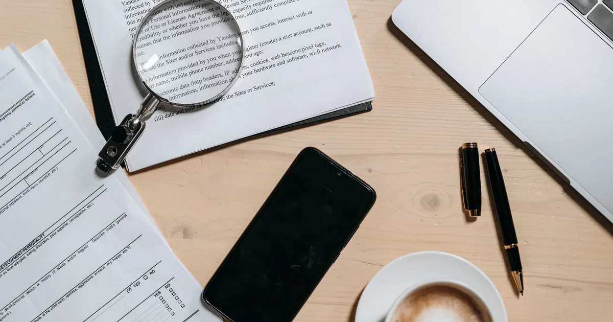 Documentos impressos empilhados ao lado de um notebook aberto